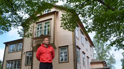 En man i rött står framför ett stort gult hus.