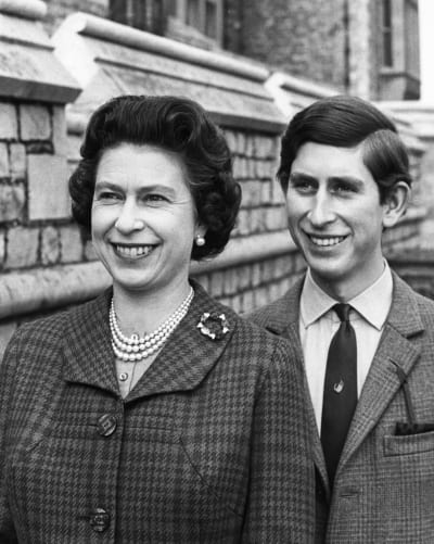 En medelålders drottning Elizabeth och ung prins Charles på en svartvit bild. Båda ser glada ut och drottningen bär ett pärlhalsband i tre rader. 