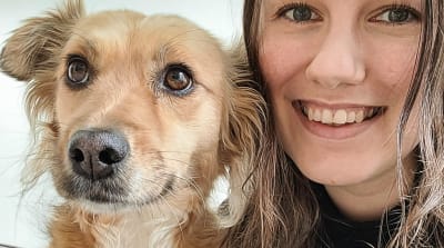 En glad, leende kvinna som tittar in i kameran med en hund. 