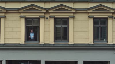 Bild utifrån på Roy Andersson som står i ett av fönstren i huset där hans studio finns. 