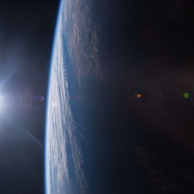 Auringonlasku kuvattuna avaruudesta. Kuvan vasemmassa laidassa on pieni kirkas aurinko ja oikealla iso maapallo.