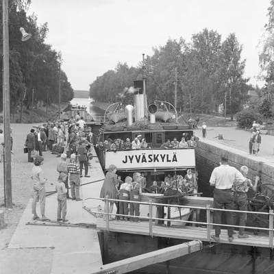 Svartvit bild: Ångbåten S/S Jyväskylä i Vääksy kanal, omgiven av stor folksamling.