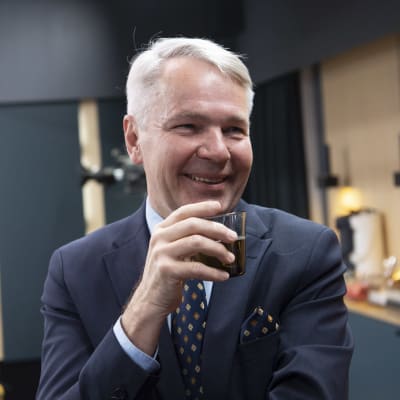 Leende man i kostym i förgrunden. Utrikesminister Pekka Haavisto (Gröna) dricker kaffe.
