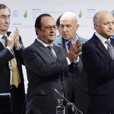 Ranskan presidentti Francois Hollande (kuvassa keskellä) ja maan ulkoministeri Laurent Fabius (oikealla)taputtavat käsiään ilmastosopimuksen julkistamisen jälkeen Pariisissa 12. joulukuuta.
