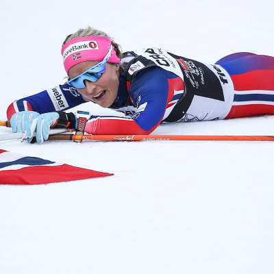 Therese Johaug ligger på snön med Norges flagga.