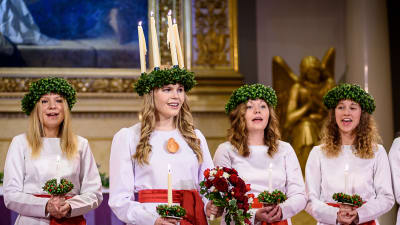 Finlands Lucia 2016 Ingrid Holm iklädd ljuskrona och vit luciadräkt med tärnor i Helsingfors domkyrka.