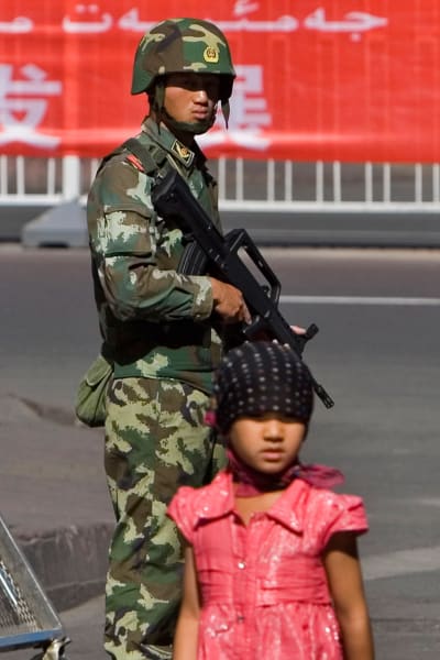 En uigurisk flicka går förbi kinesiska soldater