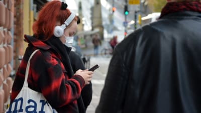 En kvinna kollar i mobilen med munskydd på, på auragatan i Åbo.