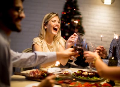 En kvinna skrattar och skålar vid ett julbord med sina vänner.