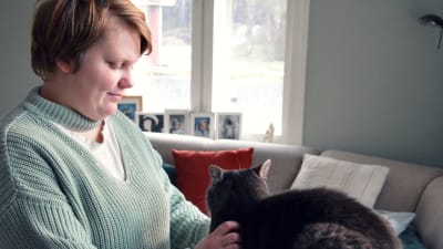 Alexandra Valkama står och klappar sin katt i ett vackert grågrönt vardagsrum.