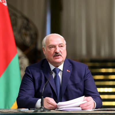 Valko-Venäjän presidentti Aljaksandr Lukašenka puhuu mikrofoniin pöydän ääressä papereita kädessään.