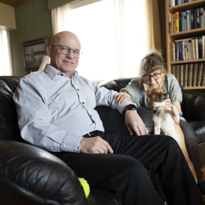 Mies istuu sohvatuolilla vaimonsa ja koiransa vierellä