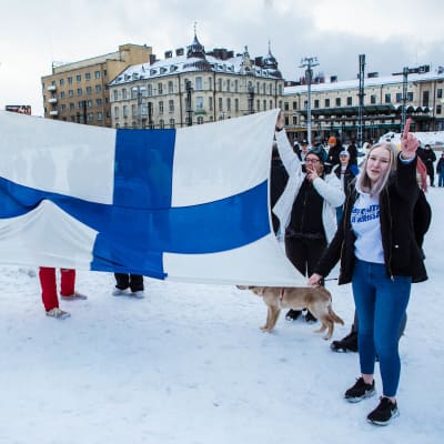 Ihmisiä levitetyn Suomen lipun kanssa juhlimassa Tampereen keskustorilla juhlimassa Suomen voittoa Venäjästä jääkiekon Pekingin olympialaisten finaalissa.  