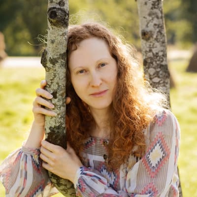 Porträtt av en kvinna (författare Erica Håkans från Vasa) som lutar huvudet mot ett träd. 