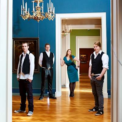 Kolme miestä ja yksi nainen seisovat rennossa muodostelmassa tilasarjassa joka muodostuu huvilan eri salien peräkkäisistä ovista.