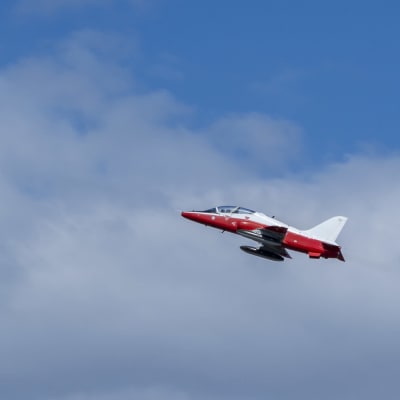 Punavalkoinen Suomen ilmavoiminen tunnuksilla varustettu Hawk hävittäjäkone lentää pilvisellä taivaalla.