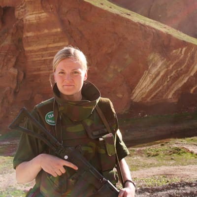 Kvinna i militärutrustning med berg i bakgrunden.