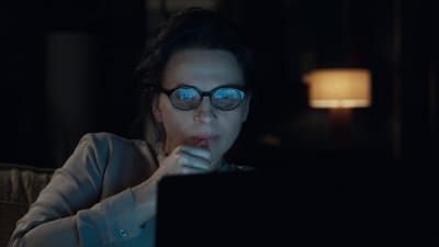 Juliette Binoche som Claire sneglar på sin datorskärm i mörkret.