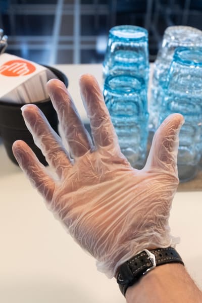  Handen har en plasthandske. Folk ombeds att använda dem när de äter på Yles lunchrestauranger.