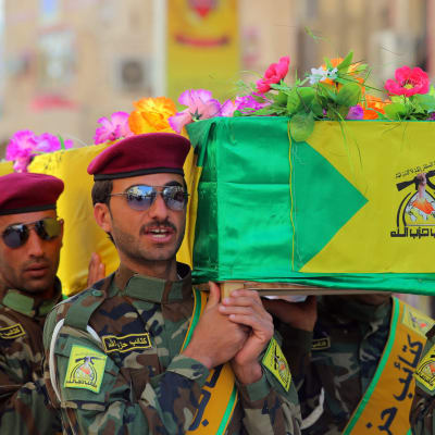 En arkivbild på milismän från Kataib Hizbollah och en kista prydd med deras flagga. Bilden är tagen under en begravning 2015 då många av milismännen dog i strider mot IS i Irak. 