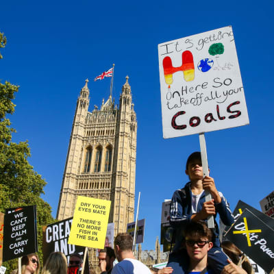 En klimatdemonstrant i London med ett plakat med texten "it's getting hot in here, so take off all your coals".
