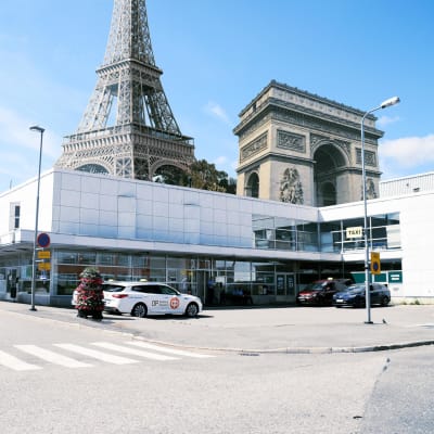 Fotomontage. Låg vit byggnad med Eiffeltornet och Triumfbågen i bakgrunden.