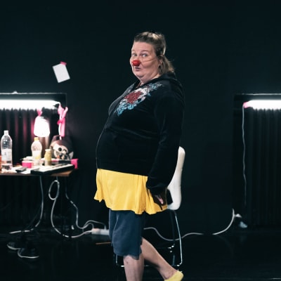 En kvinna med clownnäsa tittar in i kameran.  