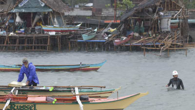 Översvämningar i Legazpi City i Filippinerna. En person hanterar en båt, en annan går omkring i vatten som når upp till midjan.