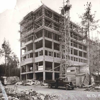 Seitsenkerroksinen asuintalo rakenteilla vuonna 1945 etualalla työmaata ja kuorma-auto.