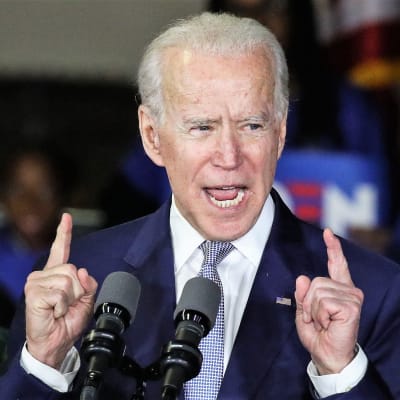 Biden puhuu osoittaen sormillaan ylöspäin. Hänellä on tummansininen puku. Taustalla näkyy Bidenin kannattajia.