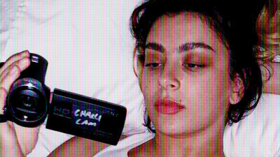 Artisten Charli XCX ligger på sängen med en kamera i handen