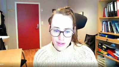 Stephanie Borenius, en dam med glasögon och en vit, norsk tröja, sitter på ett kontor med en bokhylla.