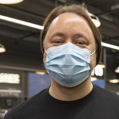 En anställd vid elektronikaffären Gigantti som står inne i butiken med munskydd på sig. Personen har en t-skjorta på sig där det står "black friday".