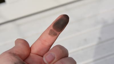 En person håller upp sitt pekfinger och man ser att undersidan av fingret är svart.