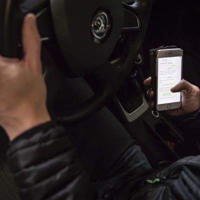 Autoilijan toinen käsi on ratilla ja toinen käyttää älypuhelinta. 