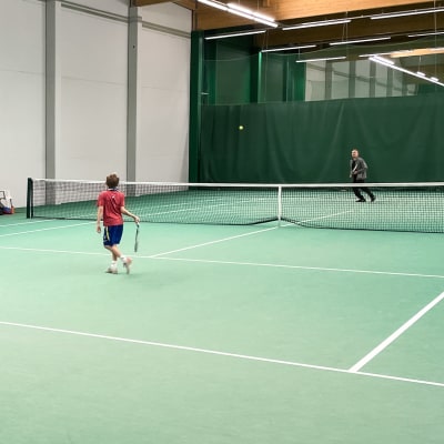 Två familjemedlemmar spelar tennis i en hall i Helsingfors.