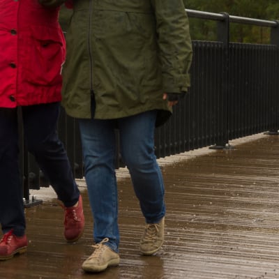 Kaksi naista kävelee sateessa sillalla.