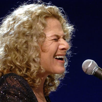 Carole King sjunger i en mikrofon.