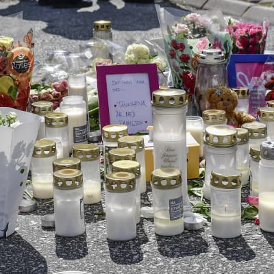 Flickor kramar och tröstar varandra framför ljus och blommor som förts till bensinstationen där en 12-årig flicka blev skjuten. 
