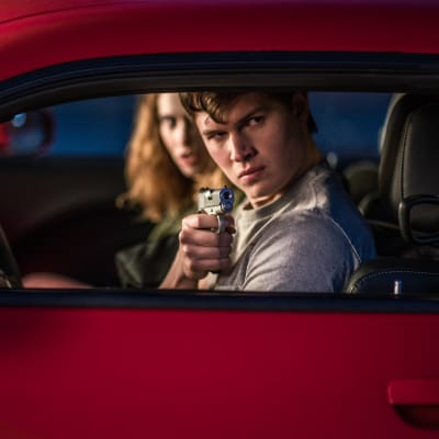 Baby (Ansel Elgort) och Debora (Lily James) sitter i en bil och Baby siktar med en pistol ut genom bilfönstret.
