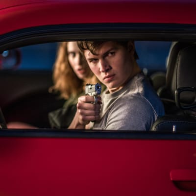 Baby (Ansel Elgort) och Debora (Lily James) sitter i en bil och Baby siktar med en pistol ut genom bilfönstret.
