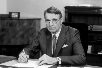President Mauno Koivisto sitter vid ett bord och undertecknar ett papper.
