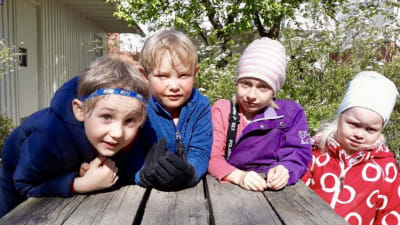 Fyra barn i dagisåldern vid ett bord utomhus.