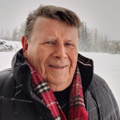 Mies katsoo kameraan, taustalla luminen maisema.