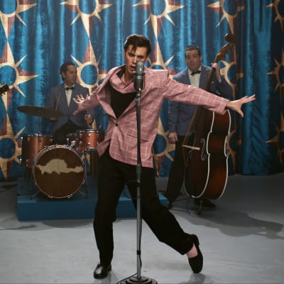 Elokuvahahmo Elvis tanssii mikrofonin edessä lavalla, taustalla yhtye.