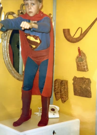 Tero Puha lapsena seisomassa valkoisen lipaston päällä, yllään Supermiesasu.