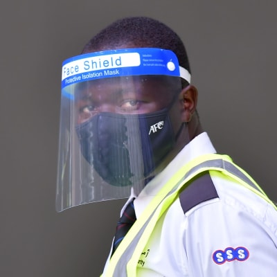 En säkerhetsvakt i munskydd och visir tittar mot sidan.