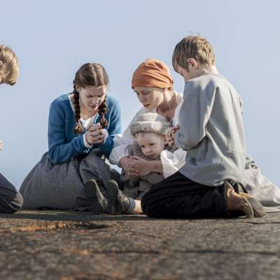 Elokuvasta Myrskyluodon Maija. Kolme poikaa ja teini-ikäinen tyttö sekä äiti rukoilevat kallioluodolla. Heillä on 1800-luvun vaatteet. Pienin lapsi on äidin sylissä.