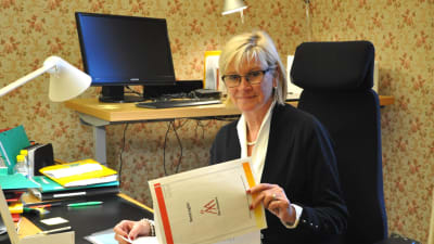 Ulla sitter vid sitt skrivbord och bläddrar i papper.
