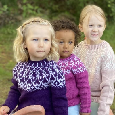 Tre flickor iklädda handstickade strömsötröjor i barnstorlekar
